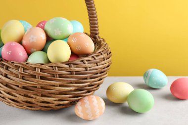 Beyaz masadaki sepetteki güzel Paskalya yumurtaları sarı arka planda, yakın plan. Metin için boşluk