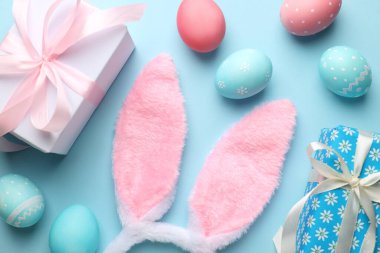 Mutlu Paskalyalar. Şirin tavşan kulakları, hediye kutuları ve açık mavi arka planda boyanmış yumurtalar, düz yatış.
