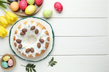 Lezzetli Paskalya pastası, boyanmış yumurtalar, sarı laleler ve beyaz ahşap masa üzerindeki yapraklar, düz yatak. Metin için boşluk