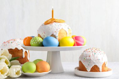 Lezzetli Paskalya pastaları, açık gri masada boyanmış yumurtalar ve laleler.