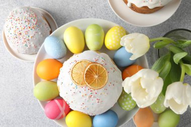 Lezzetli Paskalya pastaları, laleler ve açık gri masaya boyanmış yumurtalar.