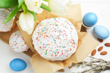 Lezzetli Paskalya pastaları, boyanmış yumurtalar, söğüt dalları ve beyaz ahşap masadaki laleler, düz yataklar.