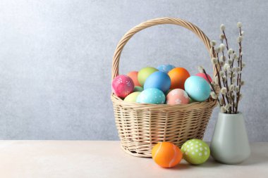 Hasır sepete boyanmış Paskalya yumurtaları ve bej masaya söğüt dalları, metin için yer