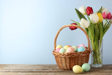 Hasır sepete boyanmış Paskalya yumurtaları ve açık mavi arkaplan ile ahşap masada güzel laleler.