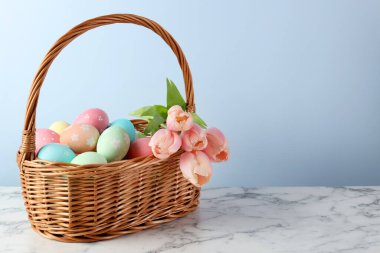 Boyanmış Paskalya yumurtaları ve hasır sepetteki güzel laleler beyaz mermer masa üzerinde, metin için yer var.