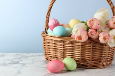 Boyanmış Paskalya yumurtaları ve hasır sepetteki güzel laleler beyaz mermer masa üzerinde, yakın plan. Metin için boşluk