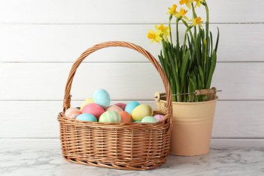 Hasır sepete boyanmış Paskalya yumurtaları ve beyaz mermer masa üzerinde güzel nergisler.