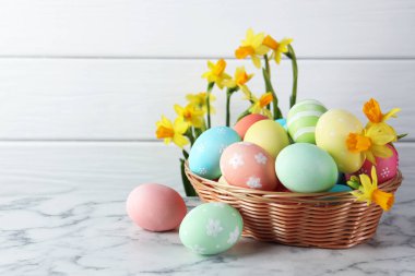 Hasır sepetin içine boyanmış Paskalya yumurtaları beyaz mermer masa ve güzel nergisler, yakın plan. Metin için boşluk
