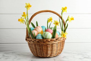 Boyanmış Paskalya yumurtaları ve beyaz mermer masanın üzerinde hasır sepetin içindeki güzel nergisler.