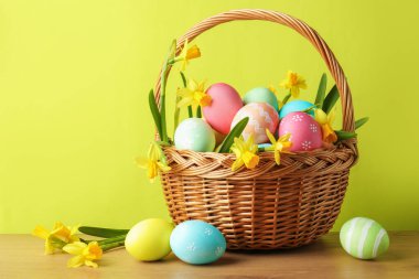 Boyanmış Paskalya yumurtaları ve ahşap masada açık yeşil arka planda hasır sepetin içindeki güzel nergisler.