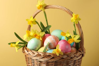 Boyanmış Paskalya yumurtaları ve bej arka planda hasır sepetin içindeki güzel nergisler, yakın plan.