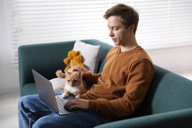 Evdeki kanepede dizüstü bilgisayar kullanan sevimli kedisi olan adam.
