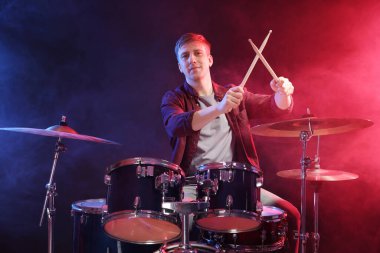 Davul çalan adam renk ışıklarıyla davul çalıyor ve siyah arkaplanda sigara içiyor