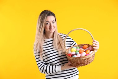 Paskalya kutlaması. Sarı arka planda boyanmış yumurta dolu sepeti olan gülümseyen kadın.