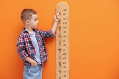 Küçük çocuk turuncu duvarın yanında boyunu ölçüyor.