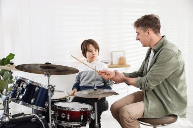 Küçük çocuk içeride müzik öğretmeniyle davul çalmayı öğreniyor.