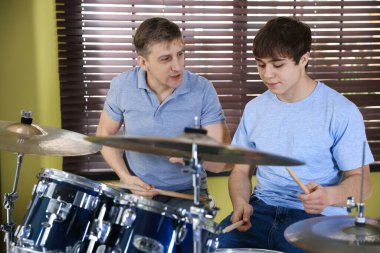 Genç çocuk içeride müzik öğretmeniyle bateri çalmayı öğreniyor.