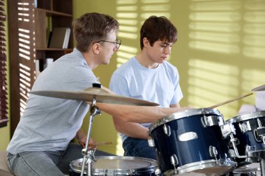 Genç çocuk içeride müzik öğretmeniyle bateri çalmayı öğreniyor.