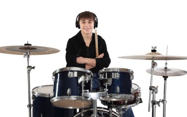 Kulaklıklı, davul setiyle beyaz arka planda gülümseyen genç bir çocuk.