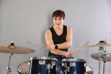 Gri arka planda davul çalmayı öğrenen güler yüzlü genç çocuk.