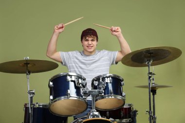 Beyzbol şapkalı gülümseyen genç, bagetleriyle yeşil arka planda davul çalmayı öğreniyor.