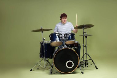 Beyzbol şapkalı gülümseyen genç, bagetleriyle yeşil arka planda davul çalmayı öğreniyor.