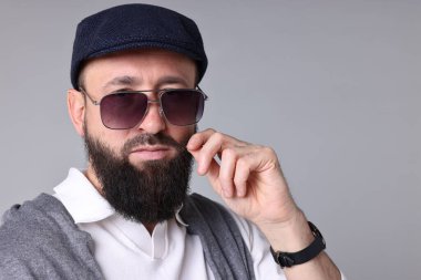 Açık gri arka planda bıyıklı ve sakallı bir adam.