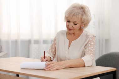 Ahşap masada son dilek ve vasiyetnameyi imzalayan üst düzey bir kadın.
