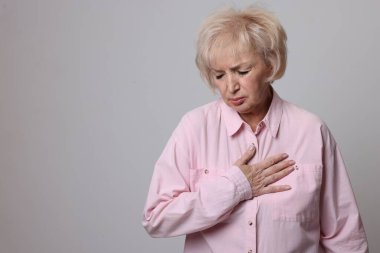 Kalp krizi geçirdi. Gri arka planda göğüs ağrısı çeken yaşlı bir kadın. Metin için boşluk