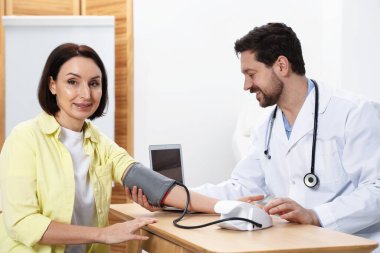 Doktor, klinikteki tahta masada hastanın kan basıncını sphygmomanometre ile ölçüyor.