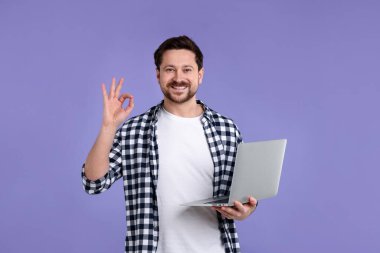 Dizüstü bilgisayarı olan bir adam mor arka planda iyi bir hareket gösteriyor