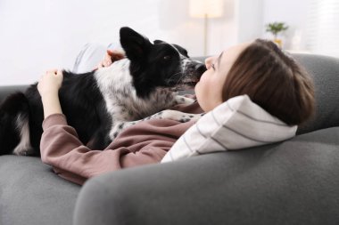 Evdeki kanepede sevimli köpeğiyle yatan bir kadın.