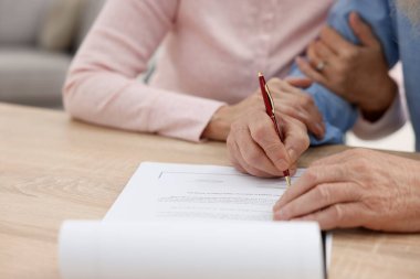 Ahşap masada son arzuları ve vasiyetnameleri imzalayan yaşlı çift, yakın plan.