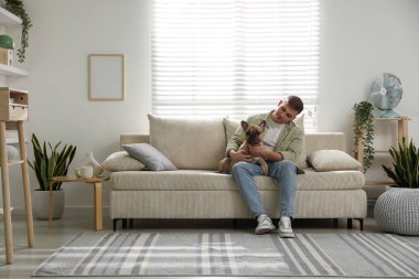 Evdeki kanepede dinlenen sevimli köpeğiyle genç bir adam.