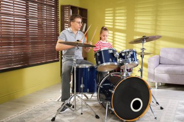 Küçük kız içeride müzik öğretmeniyle davul çalmayı öğreniyor.