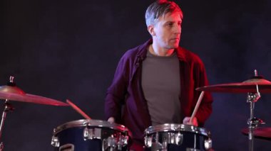 Davul çalan adam, siyah arkaplan karşısında renkli ışık ve dumanla davul çalıyor.