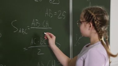 Okullu kız sınıfta tahtada matematik yapıyor.