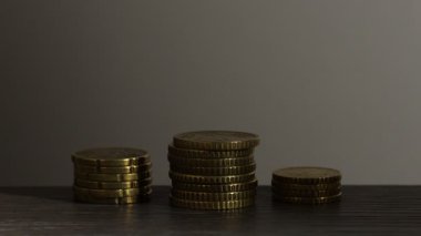 Gri arka plana karşı ahşap masada yığınla bozuk para, yakın plan. Işığın yönü değiştiriliyor