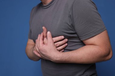 Kalp krizi geçirdi. Mavi arka planda göğüs ağrısı çeken adam, yakın plan.