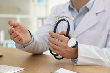 Klinikteki ahşap masada steteskop kullanan bir tıp çalışanı.