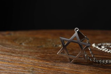 Soykırım Anma Günü. Davut Yıldızı şeklindeki kolye ve ahşap masada siyah arka planda metal zincir, yakın plan. Metin için boşluk
