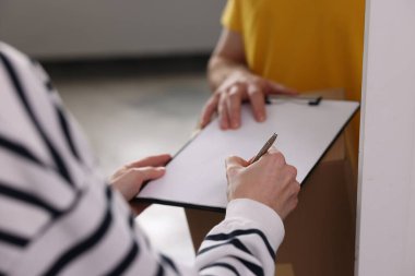 Kapalı alanda paket alırken belgeyi imzalayan kadın, kapat