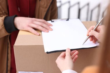 Açık havada paket alırken belgeyi imzalayan kadın, kapatma