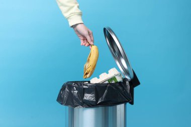 Açık mavi arka planda muz kabuğu atan kadın, yakın plan.