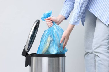 Açık gri arka planda çöp kutusundan plastik poşet çıkaran kadın, yakın plan.