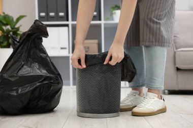 Kapalı alandaki çöp kutusuna plastik poşet koyan kadın.