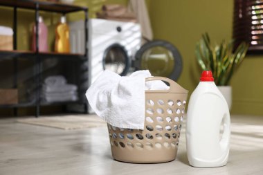Çamaşır sepetinin içinde giysiler ve yerde deterjan var. Metin için boşluk