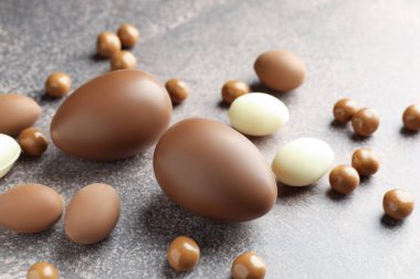 Paskalya kutlaması. Gri desenli masada bir sürü çikolata yumurtası ve dragee, yakın plan.