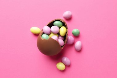Chocolate Easter egg with candies on pink background, flat lay