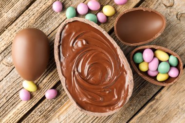 Tahta masanın üzerinde renkli şekerlemeli leziz çikolatalı yumurtalar, düz yatak. Mutlu Paskalyalar